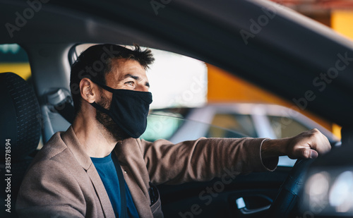 Young happy attractive fashionable man with protective face mask on driving his car during corona virus outbreak. © Sanja