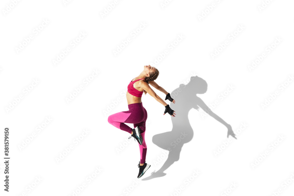 Butterfly. Beautiful young female athlete practicing on white studio background, portrait with shadows. Sportive fit model in motion and action. Body building, healthy lifestyle, style concept.
