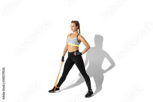 Training. Beautiful young female athlete practicing on white studio background, portrait with shadows. Sportive fit model in motion and action. Body building, healthy lifestyle, style concept. © master1305