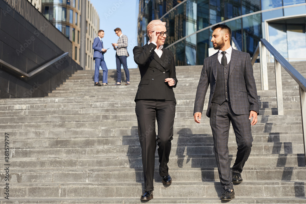 Mature businesswoman talking to businessman while they moving down the stairs outdoors Mature businesswoman talking to businessman while they moving down the stairs outdoors