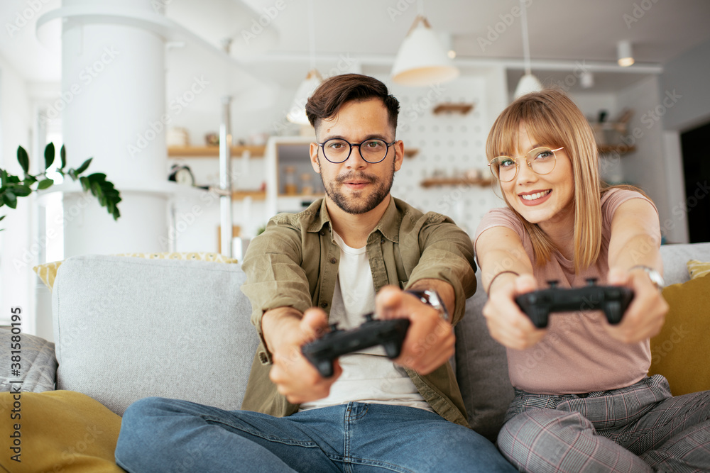 Boyfriend and girlfriend playing video game with joysticks in living room. Loving couple are playing video games at home... Boyfriend and girlfriend playing video game with joysticks in living room. Loving couple are playing video games at home...