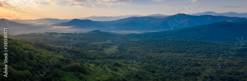 Early morning in the mountains. Morning sun and haze in the valley against the background of mountains. Mountain summer landscape. Banner size © Alexey Oblov