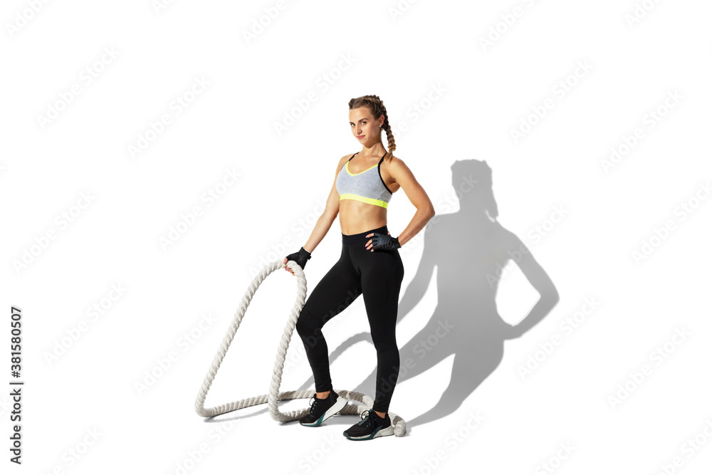 Ropes. Beautiful young female athlete practicing on white studio background, portrait with shadows. Sportive fit model in motion and action. Body building, healthy lifestyle, style concept. Ropes. Beautiful young female athlete practicing on white studio background, portrait with shadows. Sportive fit model in motion and action. Body building, healthy lifestyle, style concept.