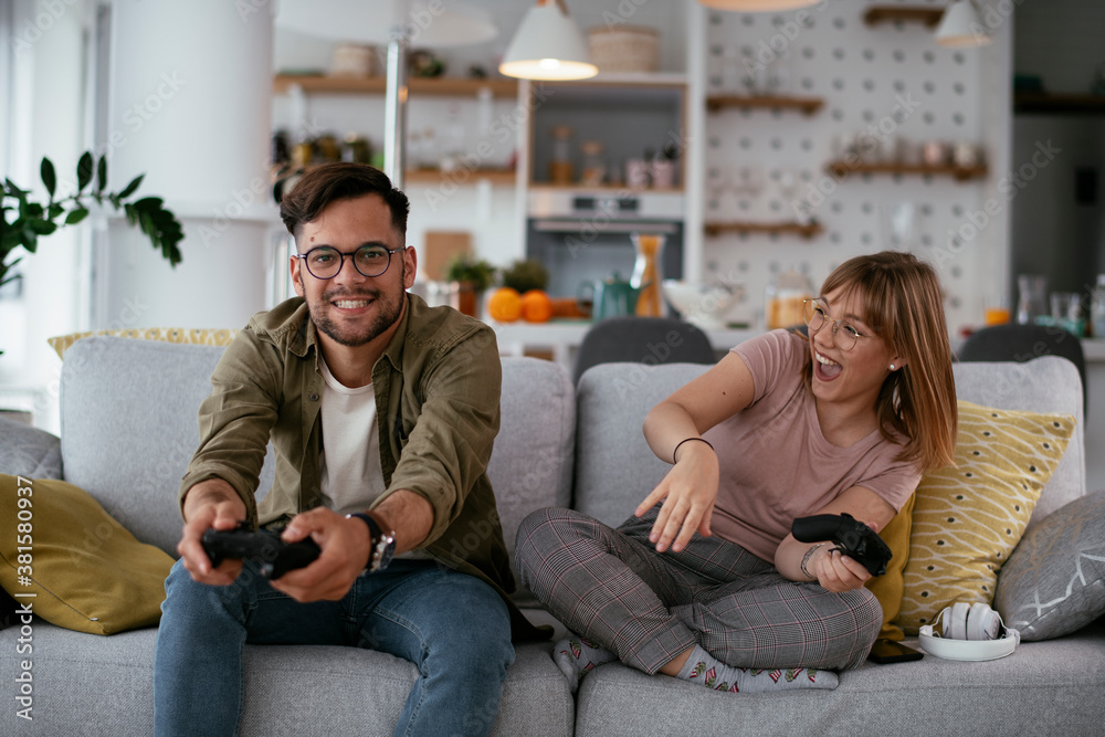Boyfriend and girlfriend playing video game with joysticks in living room. Loving couple are playing video games at home...