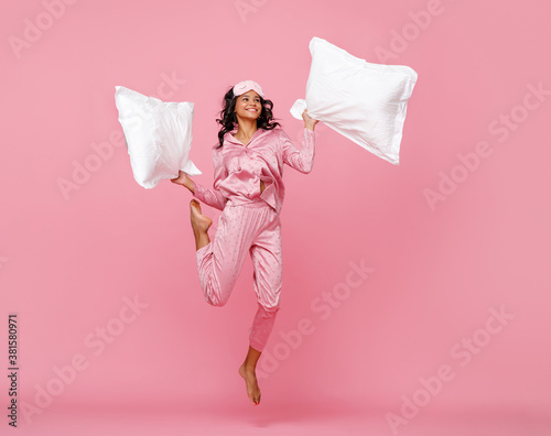 Excited woman in pajama jumping with pillow