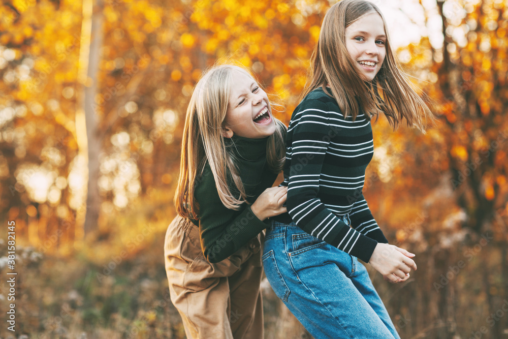 Two happy girls sisters laughing, having fun and playing in the fall in nature outdoors in the autumn park