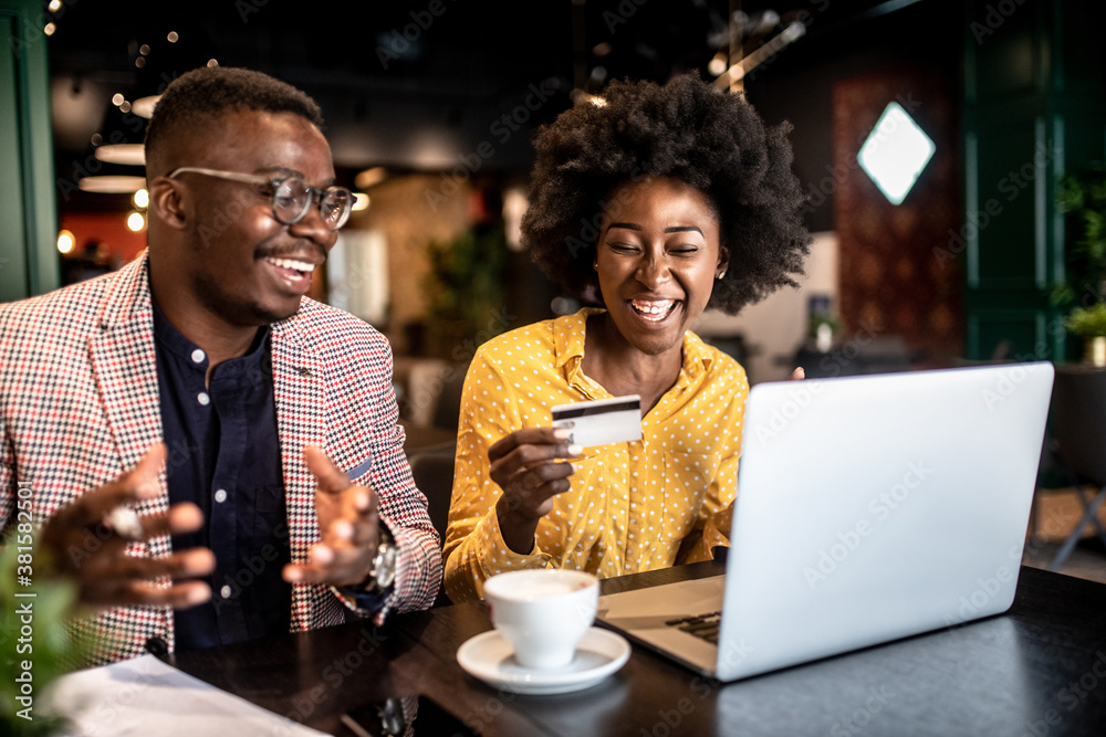 Attractive smiling african couple sitting in cafe and purchasing over internet things for house.