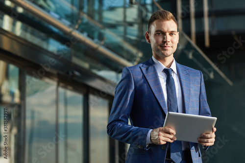Portrait of young businessman in formal suit looking at camera while using digital tablet in the city