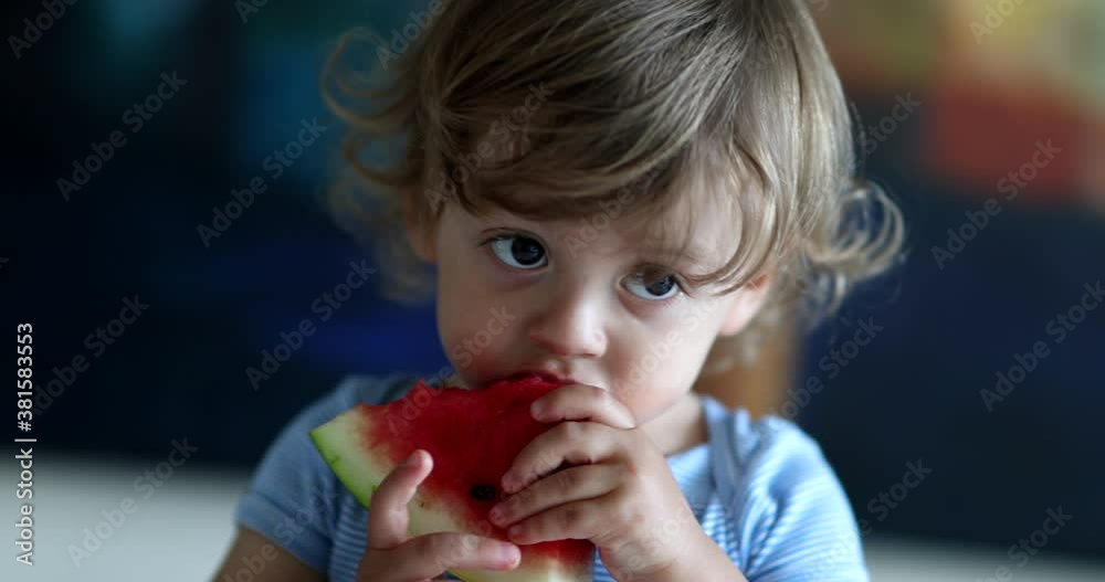 Toddler eating watermelon fruit. Close-up child taking a bite of juicy watermelon Toddler eating watermelon fruit. Close-up child taking a bite of juicy watermelon