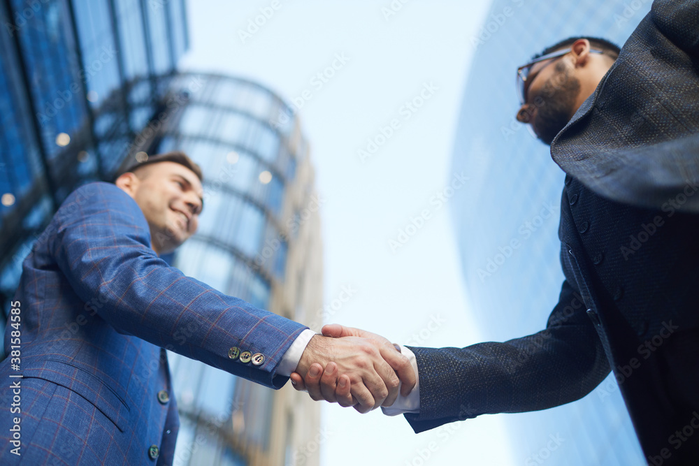 Low angle view of two young businessmen shaking hands during their meeting in the city