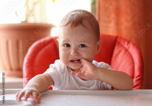 Adorable little baby boy sits in the highchair and chews his fingers. Baby teething.