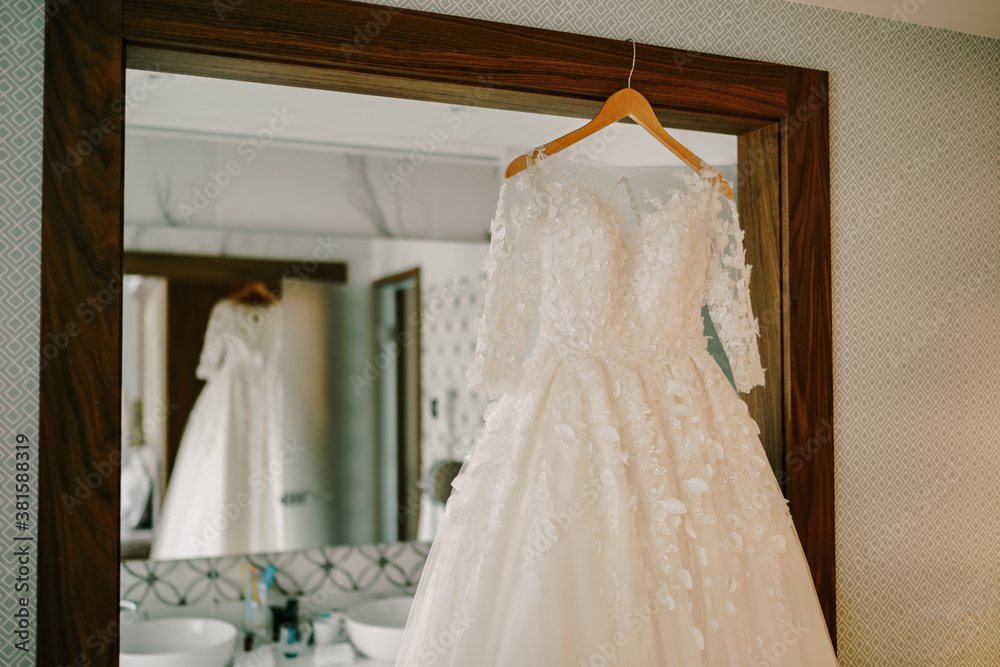 Lush wedding dress on a wooden hanger by the mirror.