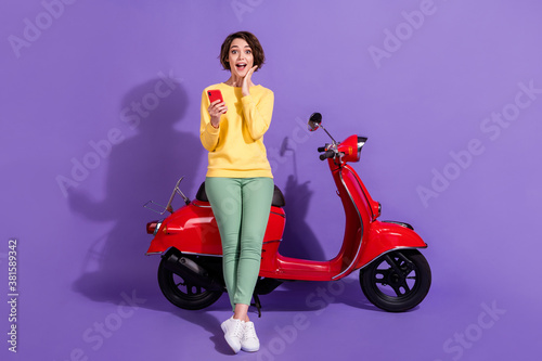 Full length body size view attractive amazed stunned cheerful glad girl sitting on bike using device browsing post app 5g isolated over bright vivid shine vibrant lilac violet purple color background