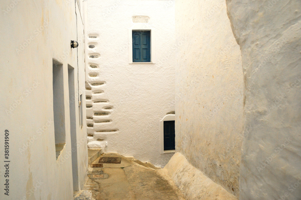 Wąska uliczka na greckiej wyspie Amorgos. Białe ściany, niebieskie okna.