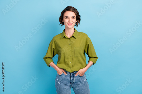 Photo of pretty confident lady short hairstyle happy cheerful look camera hands pockets wear denim jeans green shirt isolated blue color background