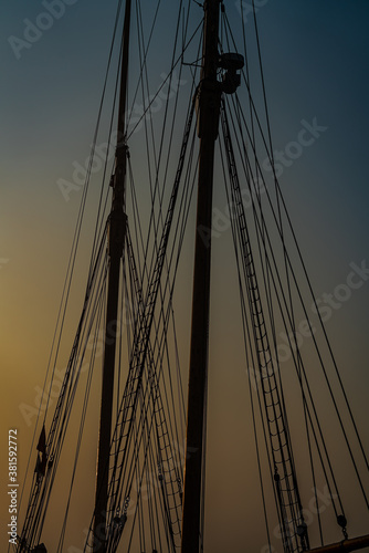 Mast and rigging of an old wooden tall ship, silhouette against the morning light and mist.