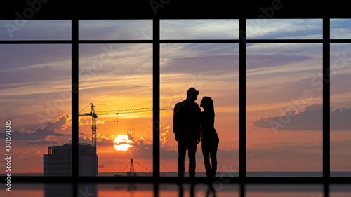 The couple standing near the panoramic window against the city sunset
