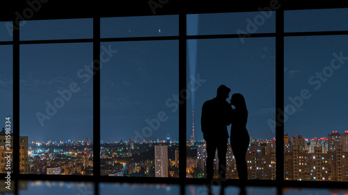 The couple standing near the panoramic window on the city background
