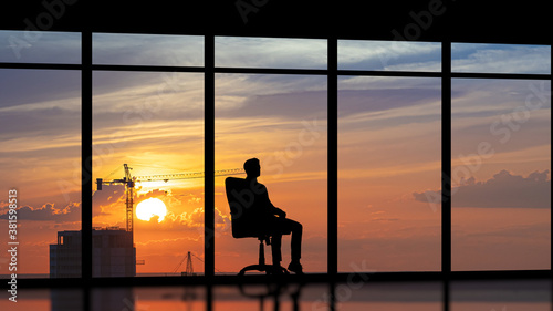 The man sitting near a panoramic window against the city sunset © realstock1