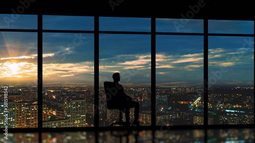 The male sitting near the panoramic window on the city sunset background