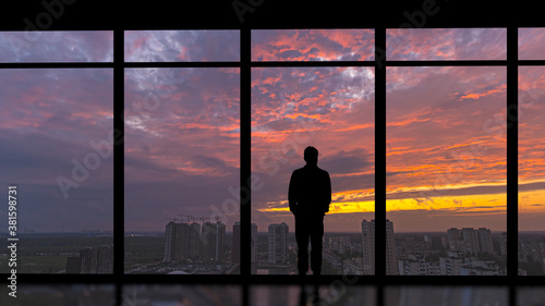 The man standing near the panoramic window on the city sunset background © realstock1