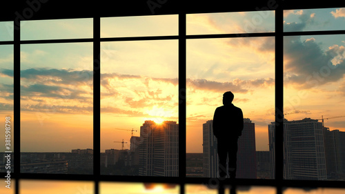 The male standing near the panoramic window against the beautiful city sunset