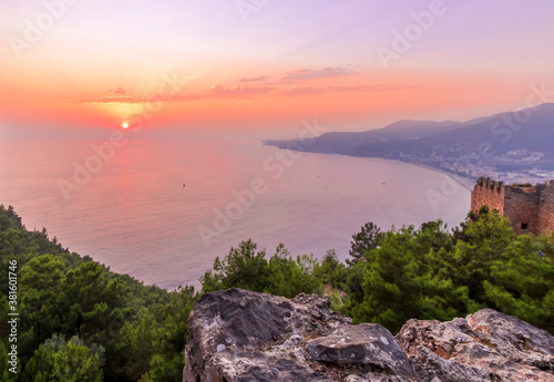 scenic view at picturesque sunset from high mountain with bushes and green trees below and beautiful cloudy sky, sea with far coast, sun glow with reflection on the background , castle landscape