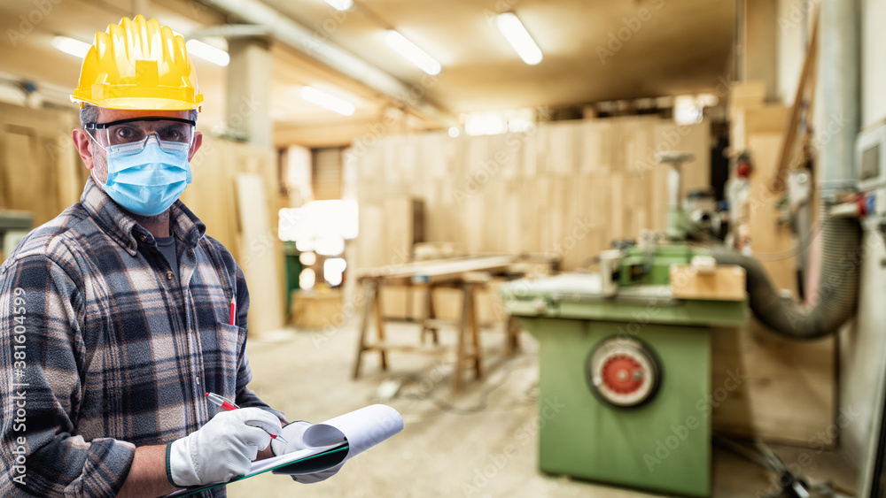 Carpenter worker in the carpentry workshop, wears helmet, goggles, leather gloves and surgical mask to prevent coronavirus infection. Preventing Pandemic Covid-19 at the workplace. Carpenter worker in the carpentry workshop, wears helmet, goggles, leather gloves and surgical mask to prevent coronavirus infection. Preventing Pandemic Covid-19 at the workplace.