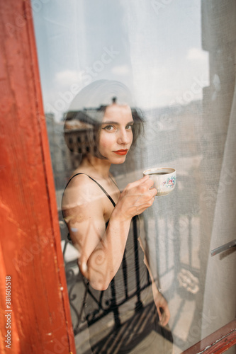 young beautiful woman with a cup of fragrant coffee standing by the window © Victoriya Bulyha