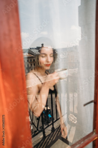 young beautiful woman with a cup of fragrant coffee standing by the window © Victoriya Bulyha