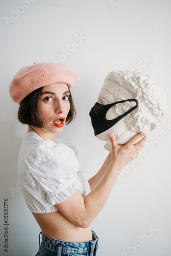 young stylish woman in a beret with a sculpture in a mask, the new normality
