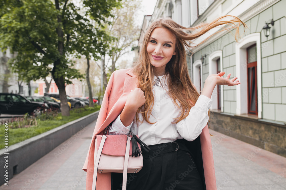 attractive stylish smiling woman walking city street in pink coat spring fashion trend holding purse, elegant style, waving long hair attractive stylish smiling woman walking city street in pink coat spring fashion trend holding purse, elegant style, waving long hair