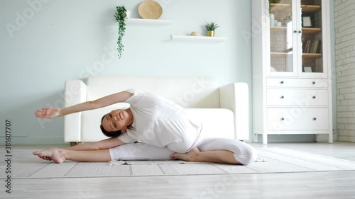 Attractive pregnant lady in white clothes does janu sirsasana position sitting on floor with rug against designer couch in spacious room at home photo