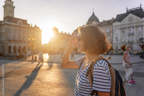 Young woman traveler with a backpack standing at sunset on the square in a European city