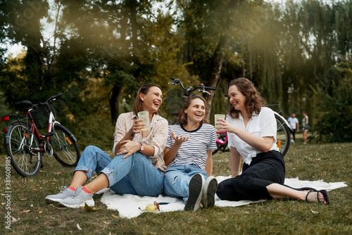 Three beautiful happy young women close friends relax in a green park on a blanket. Have fun laughing and chatting on the green grass.