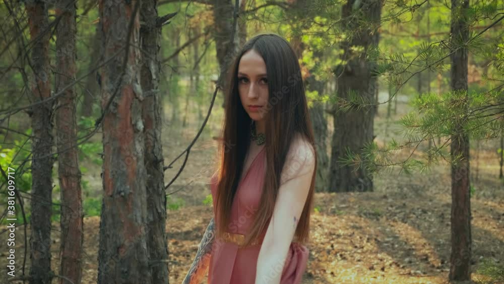 Portrait of a beautiful young woman forest nymph. The attractive girl elf walks in the autumn forest. Rear view from the back, turns and looks at camera. Creative sexy fantasy style silk pink dress Portrait of a beautiful young woman forest nymph. The attractive girl elf walks in the autumn forest. Rear view from the back, turns and looks at camera. Creative sexy fantasy style silk pink dress