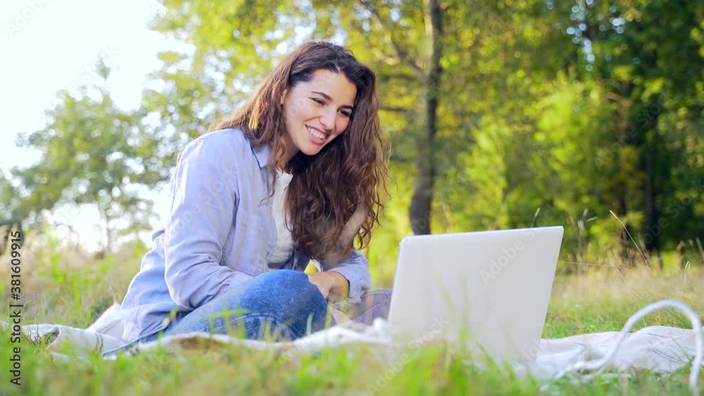 Portrait Student Girl Studying and Working Online Using Laptop and Notebook in Nature Park on Lawn. Young Hipster Woman Communicates Remotely via Webcam Chat Waving Hand at Screen. Distance Learning Portrait Student Girl Studying and Working Online Using Laptop and Notebook in Nature Park on Lawn. Young Hipster Woman Communicates Remotely via Webcam Chat Waving Hand at Screen. Distance Learning