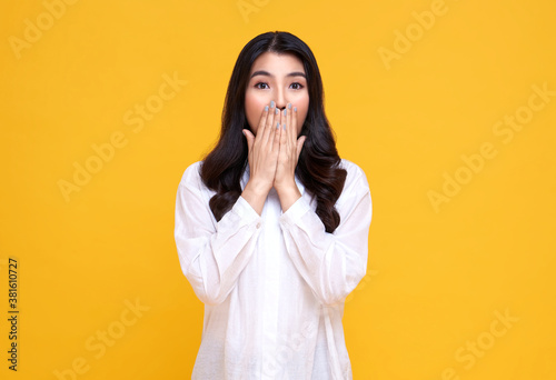 Фотография Surprised and Shocked asian woman covering mouth with hands isolated on bright yellow background