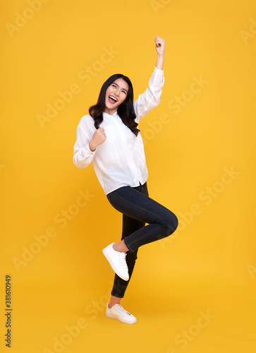 Happy Asian woman smiling and standing with hand up celebrating gesture on yellow background. © NaMong Productions