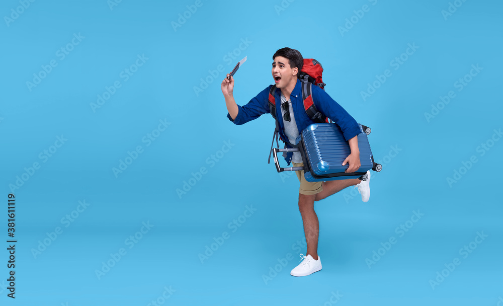 Young excited Asian man traveler running with backpack passport and boarding pass ready to fly on isolated blue background. Young excited Asian man traveler running with backpack passport and boarding pass ready to fly on isolated blue background.