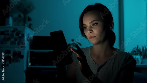 Woman scrolling mobile phone at night. Young girl read smart phone sitting on couch at home