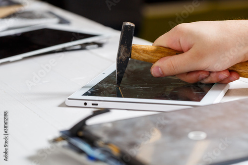 The hammer hits the broken touchscreen tablet, suggesting that it is about to replace it. Broken glass tablet repair