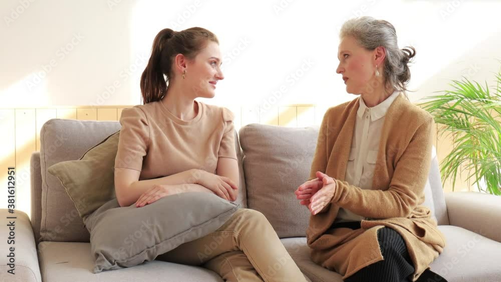 Smiling middle aged woman relaxing on couch with happy grown up daughter, talking about life moments. Smiling middle aged woman relaxing on couch with happy grown up daughter, talking about life moments.
