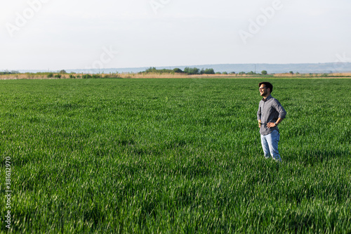 Portrait of farmer standing in young wheat field examining crop.