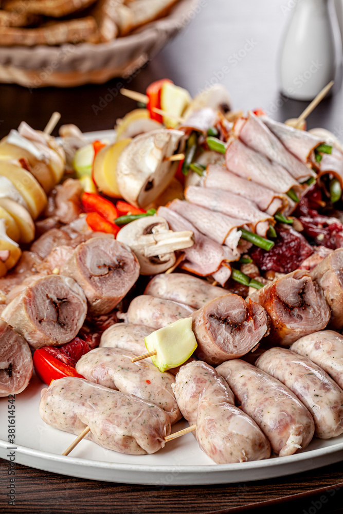 Large grill plate with raw food, sausages, barbecue, potatoes, vegetables for the company.