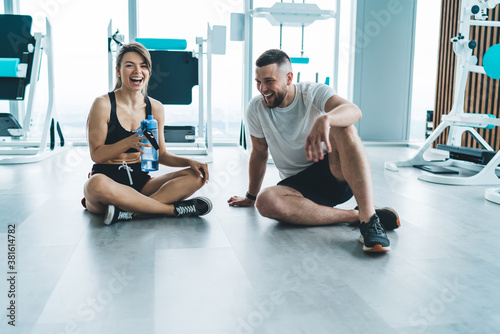Portrait of cheerful caucasian couple in love having conversation on break in gym satisfied with spending time on active hobby together  happy woman laughing at funny jokes of boyfriend resting in gym