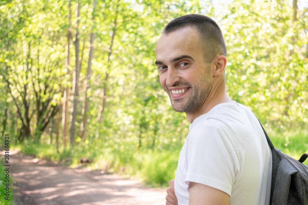Smiling traveler with a backpack walking in the forest, rear view Smiling traveler with a backpack walking in the forest, rear view