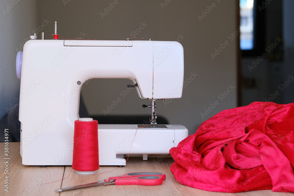 red velvet cloth, threads lie at modern sewing machine, selective focus on needle and moving parts of technology, concept of home handicraft, textile production