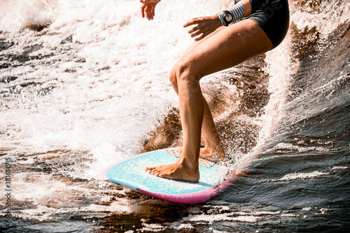 Photography close-up of athletic legs of young woman riding wave on surf style wakeboard