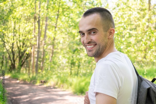 Smiling traveler with a backpack walking in the forest, rear view